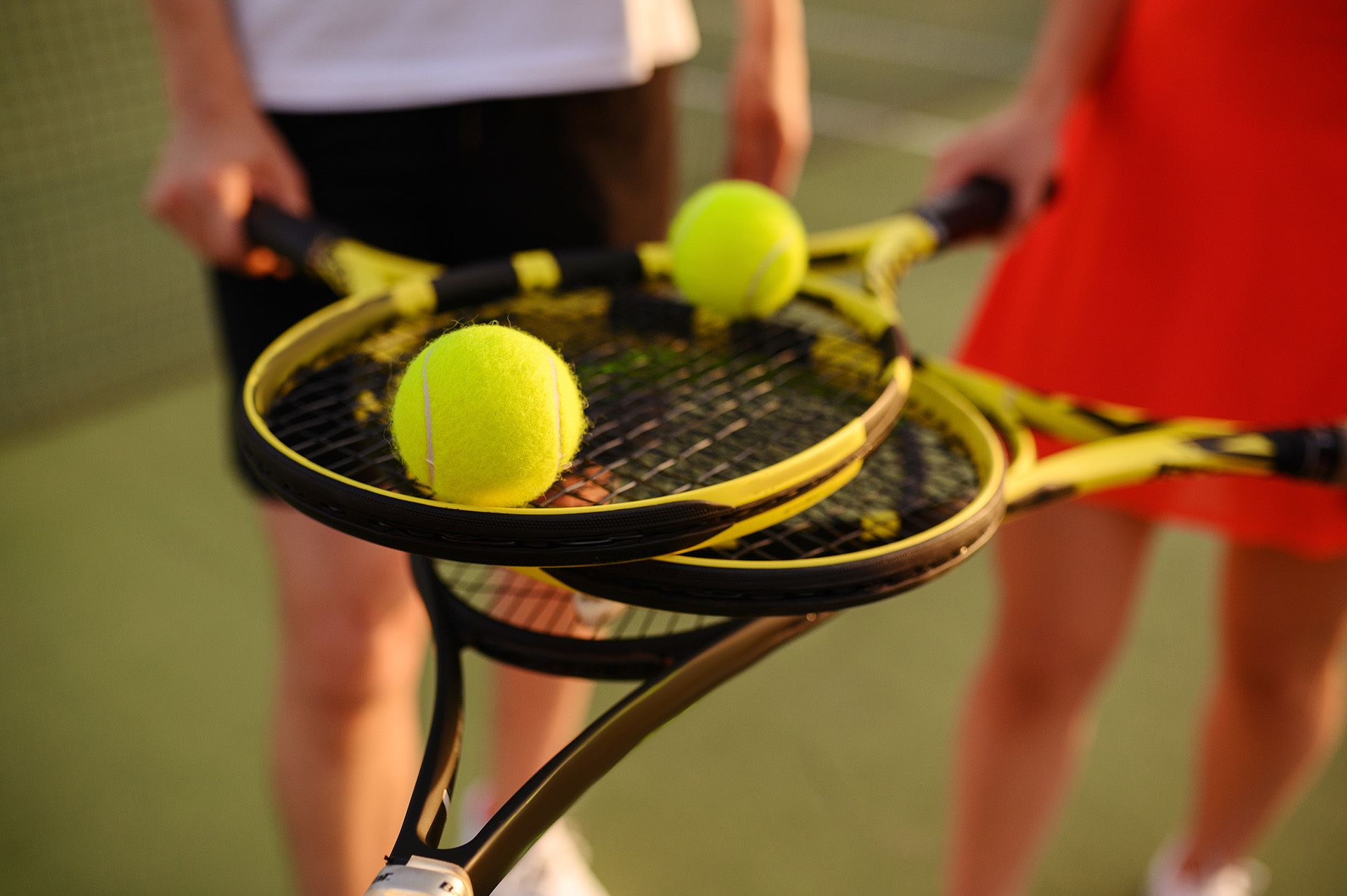 Zwei Tennisschläger mit Tennisbällen, gehalten von Spielern auf einem Tennisplatz – repräsentativ für den Tennissport und das Vereinsleben im Tennisclub Schwarz-Weiß Montabaur.
